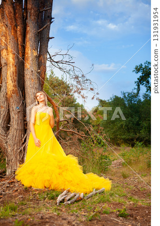 An Elegant Woman Dressed in a Beautiful Yellow Dress is Standing Gracefully by a Tree An Elegant Woman Dressed in a Beautiful Yellow Dress is Standing Gracefully by a Tree 131931954
