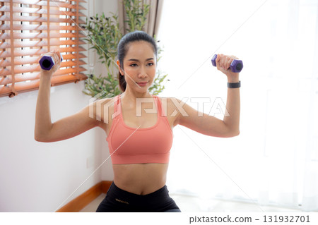 Young asian woman in sportswear workout with dumbbells for strength in living room. Young asian woman in sportswear workout with dumbbells for strength in living room. 131932701