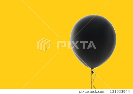 Black balloon rises against a vibrant yellow background 131933944