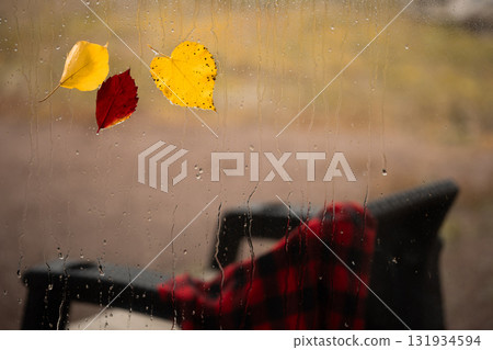 Autumn Rain Streaks Down Window With Leaves and a Chair in the Background 131934594