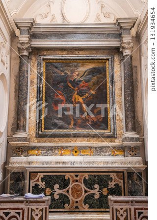 An ornate altar in an Amalfi church features a vivid religious painting framed by marble columns, intricate stonework, and colorful inlays. 131934654
