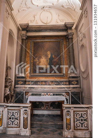 An intricately designed altar in an Amalfi church, featuring a Nativity painting, marble columns, gold accents, and a stucco ceiling with curved designs. 131934657