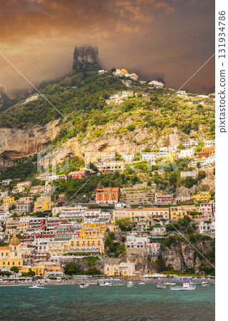Positano on Italy's Amalfi Coast features vibrant buildings cascading down a hillside, turquoise waters, rugged cliffs, and boats in a golden light. 131934786