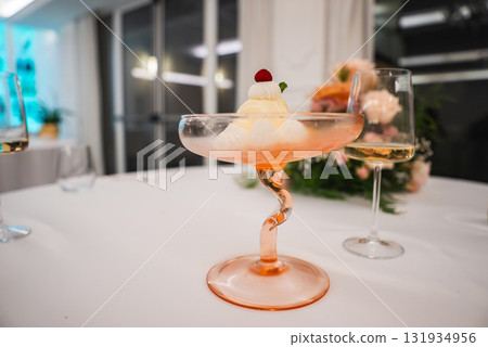 A refined dessert in a pink hued twisted stem glass, topped with a raspberry and mint leaf. Set on a white tablecloth with floral decor in Amalfi, Italy. A refined dessert in a pink hued twisted stem glass, topped with a raspberry and mint leaf. Set on a white tablecloth with floral decor in Amalfi, Italy. 131934956