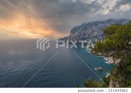 The island of Capri in Italy features steep cliffs, turquoise Mediterranean waters, and a golden sunset. Trees and white buildings frame the coastline. The island of Capri in Italy features steep cliffs, turquoise Mediterranean waters, and a golden sunset. Trees and white buildings frame the coastline. 131934962