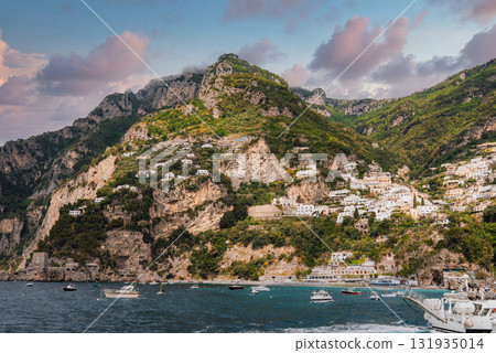 The town of Positano on Italy's Amalfi Coast features pastel buildings on steep cliffs, turquoise waters with boats, lush greenery, and a cloudy sky. The town of Positano on Italy's Amalfi Coast features pastel buildings on steep cliffs, turquoise waters with boats, lush greenery, and a cloudy sky. 131935014