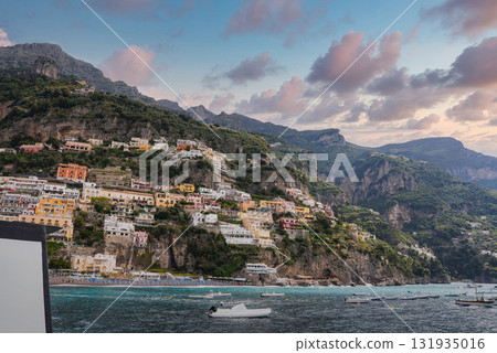 The coastal town of Positano, Italy, features cascading colorful buildings, lush cliffs, calm blue waters with boats, and a serene pink and blue sky. The coastal town of Positano, Italy, features cascading colorful buildings, lush cliffs, calm blue waters with boats, and a serene pink and blue sky. 131935016