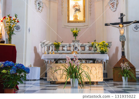 Interior of a church in Ravello, Italy, featuring an ornate altar with yellow and pink flowers, a crucifix, a Virgin Mary statue, and a checkered floor. Interior of a church in Ravello, Italy, featuring an ornate altar with yellow and pink flowers, a crucifix, a Virgin Mary statue, and a checkered floor. 131935022