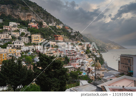 Positano on the Amalfi Coast features stacked buildings, a church dome, lush greenery, cliffs, and the Mediterranean Sea under a cloudy sky. 131935048