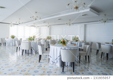 Bright dining room in Amalfi hotel featuring ornate chandeliers, patterned tiles, large windows, and round tables with floral centerpieces. 131935057