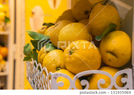 Bright yellow lemons with green leaves sit in a decorative white metal basket. A yellow wall in the background complements the citrus display. Bright yellow lemons with green leaves sit in a decorative white metal basket. A yellow wall in the background complements the citrus display. 131935069