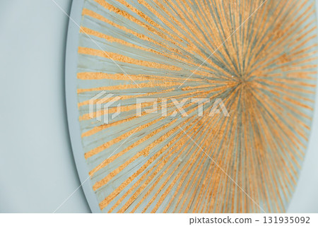A detailed circular design featuring radiant golden lines on a light blue or gray background. The metallic sheen enhances the intricate pattern. A detailed circular design featuring radiant golden lines on a light blue or gray background. The metallic sheen enhances the intricate pattern. 131935092