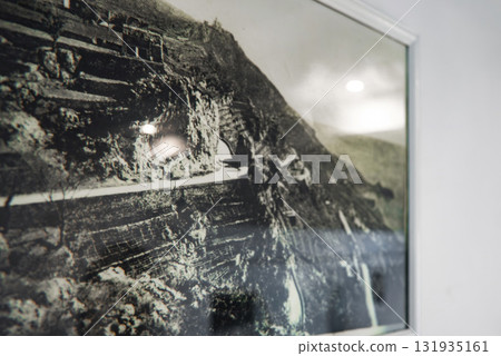 A black and white photograph of a terraced hillside with stone walls and a winding pathway, displayed indoors with reflections on the glass frame. 131935161