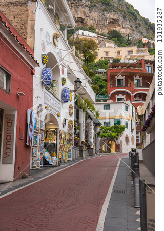 A narrow red brick street in Positano, Italy, lined with shops displaying lemon themed ceramics. White and earthy buildings sit against a steep hillside. A narrow red brick street in Positano, Italy, lined with shops displaying lemon themed ceramics. White and earthy buildings sit against a steep hillside. 131935287