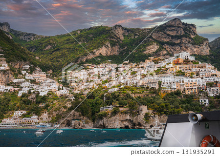 View of Positano's vibrant hillside buildings cascading to the Tyrrhenian Sea, with boats on the water and a serene orange and purple sky. View of Positano's vibrant hillside buildings cascading to the Tyrrhenian Sea, with boats on the water and a serene orange and purple sky. 131935291