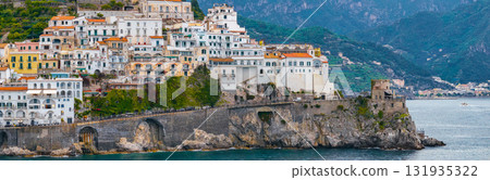 Amalfi town on Italy's Amalfi Coast, featuring tiered pastel buildings on cliffs, lush green hills, and a fortress on a rocky outcrop by the sea. Amalfi town on Italy's Amalfi Coast, featuring tiered pastel buildings on cliffs, lush green hills, and a fortress on a rocky outcrop by the sea. 131935322