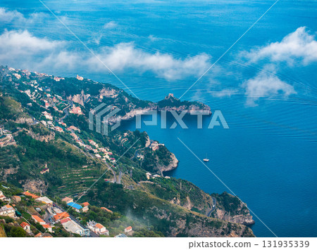Aerial view of the Amalfi Coast in Italy, showing cliffs, green hills, colorful buildings, a small bay with a boat, and the Tyrrhenian Sea below. Aerial view of the Amalfi Coast in Italy, showing cliffs, green hills, colorful buildings, a small bay with a boat, and the Tyrrhenian Sea below. 131935339