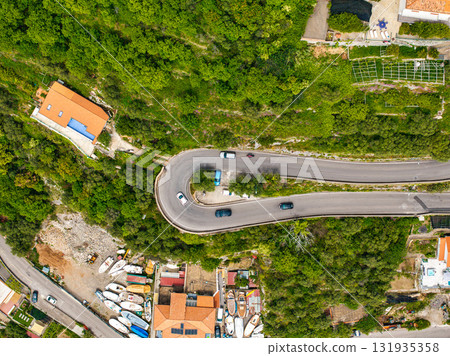 Aerial image of a sharp hairpin turn on a lush green road in Amalfi, Italy, with vehicles, orange roofed buildings, and boats near the coastline. Aerial image of a sharp hairpin turn on a lush green road in Amalfi, Italy, with vehicles, orange roofed buildings, and boats near the coastline. 131935358