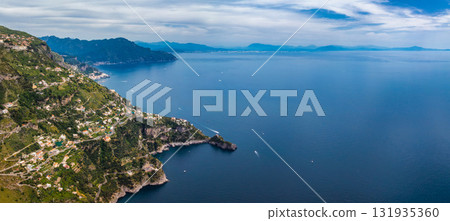 Aerial view of the Amalfi Coast in Italy, featuring cliffs, terraced hills, charming buildings, boats on the Tyrrhenian Sea, and distant mountains. Aerial view of the Amalfi Coast in Italy, featuring cliffs, terraced hills, charming buildings, boats on the Tyrrhenian Sea, and distant mountains. 131935360