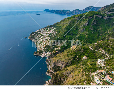 Aerial view of Amalfi, Italy, showing cliffs with greenery, terraced hills, white buildings, winding roads, and boats on the Tyrrhenian Sea. Aerial view of Amalfi, Italy, showing cliffs with greenery, terraced hills, white buildings, winding roads, and boats on the Tyrrhenian Sea. 131935362