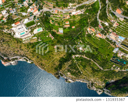 Aerial image of Amalfi town in Italy, featuring terraced hills, houses, gardens, luxury accommodations, winding roads, and the Tyrrhenian Sea. 131935367