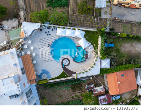 Circular pool with whirlpool section, white umbrellas, lounge chairs, lush gardens, terraced farmland, and nearby terracotta roofed buildings. Circular pool with whirlpool section, white umbrellas, lounge chairs, lush gardens, terraced farmland, and nearby terracotta roofed buildings. 131935378