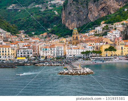Amalfi town on Italy's Amalfi Coast, featuring cascading colorful buildings, Amalfi Cathedral, a small harbor, cliffs, and the Tyrrhenian Sea. 131935381