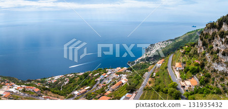 Aerial view of Amalfi, Italy, featuring cliffs with greenery, terraced vineyards, winding roads, terracotta roofed buildings, and the Tyrrhenian Sea. Aerial view of Amalfi, Italy, featuring cliffs with greenery, terraced vineyards, winding roads, terracotta roofed buildings, and the Tyrrhenian Sea. 131935432