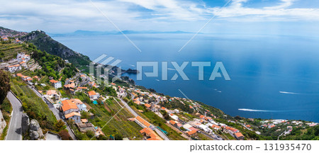 Aerial view of Amalfi, Italy, featuring terraced hills, whitewashed buildings, winding roads, and boats on the deep blue Tyrrhenian Sea. 131935470