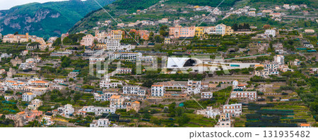 Aerial view of Ravello, Italy, featuring terraced landscapes, colorful buildings, verdant hills, and the white curved roof of the Auditorium Oscar Niemeyer. Aerial view of Ravello, Italy, featuring terraced landscapes, colorful buildings, verdant hills, and the white curved roof of the Auditorium Oscar Niemeyer. 131935482