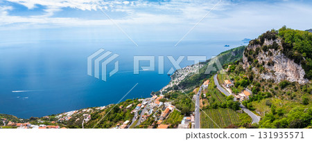Aerial view of Amalfi, Italy, featuring cliffs, terraced vineyards, winding roads, white buildings, the Tyrrhenian Sea, small islands, and boats. Aerial view of Amalfi, Italy, featuring cliffs, terraced vineyards, winding roads, white buildings, the Tyrrhenian Sea, small islands, and boats. 131935571
