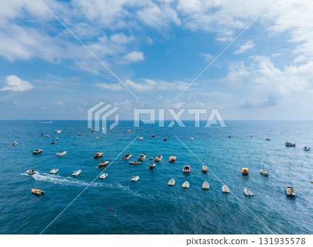 Calm blue waters near Positano, Italy, with small boats scattered across the sea. Partly cloudy sky adds depth, blending seamlessly with the horizon. 131935578