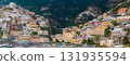 View of Positano on the Amalfi Coast, featuring colorful cliffside buildings, the Church of Santa Maria Assunta, a lively beach, and green cliffs. 131935594