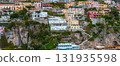 View of Positano, Italy, with vibrant buildings on steep cliffs, lush greenery, terraced gardens, and narrow pathways cascading to the coast. 131935598