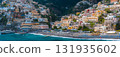 View of Positano on Italy's Amalfi Coast, featuring stacked buildings, the Church of Santa Maria Assunta, a beach with blue umbrellas, and turquoise waters. 131935602