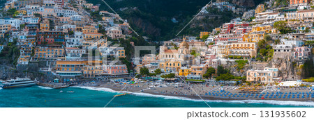 View of Positano on Italy's Amalfi Coast, featuring stacked buildings, the Church of Santa Maria Assunta, a beach with blue umbrellas, and turquoise waters. View of Positano on Italy's Amalfi Coast, featuring stacked buildings, the Church of Santa Maria Assunta, a beach with blue umbrellas, and turquoise waters. 131935602