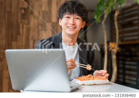 The hands of a businessman looking at a laptop while eating lunch in a cafeteria or cafe 131936460