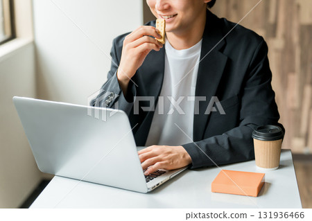 一位商人/男士在咖啡館吃零食的同時在電腦上工作 一位商人/男士在咖啡館吃零食的同時在電腦上工作 131936466