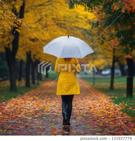 Bright yellow raincoat contrasts with autumn leaves on a rainy day in a city park 131937779