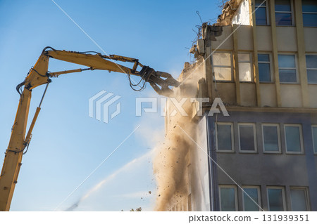 Powerful demolition of a concrete office building with a yellow high-reach excavator. Concept of transformation, destruction and construction renewal. 131939351