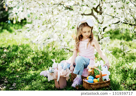 Easter egg hunt. Girl child Wearing Bunny Ears Running To Pick Up Egg In Garden. Easter tradition. Baby with basket full of colorful eggs. 131939717