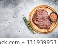 Perfectly grilled top sirloin steak, seared to a juicy finish and garnished with fresh herbs for an irresistible flavor. grey background. top view 131939953