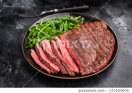 Juicy grilled top sirloin on a plate, accompanied by seasonal greens for a delicious meal. black background. top view 131939956