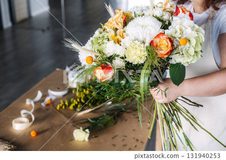 Florist tying stems of a handmade autumn bouquet on a craft table. Seasonal gifting, Thanksgiving florals, sustainable decor, creative expression Florist tying stems of a handmade autumn bouquet on a craft table. Seasonal gifting, Thanksgiving florals, sustainable decor, creative expression 131940253