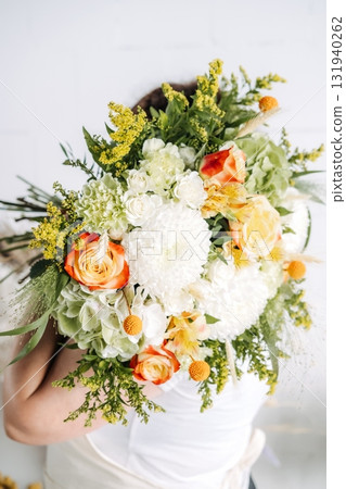 Large bouquet of mixed white and orange flowers held by a woman with arms wrapped around it. Seasonal wedding design, fall floristry, natural tones, flower artistry 131940262