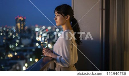一名女子站在公寓大樓的陽台上,凝視著夜景。她手捧酒杯,長髮在夜風中飄揚。 一名女子站在公寓大樓的陽台上,凝視著夜景。她手捧酒杯,長髮在夜風中飄揚。 131940786