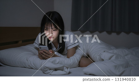 一位身穿家居服的女士躺在床上，操作著她的智慧型手機 131940810