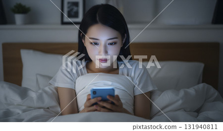 一位身穿家居服的女士躺在床上，操作著她的智慧型手機 131940811