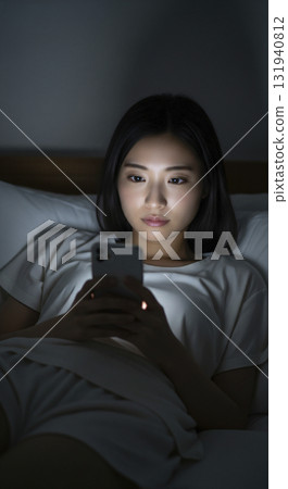 一位身穿家居服的女士躺在床上，操作著她的智慧型手機 131940812