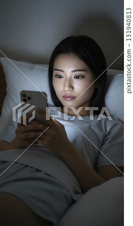 一位身穿家居服的女士躺在床上，操作著她的智慧型手機 131940813